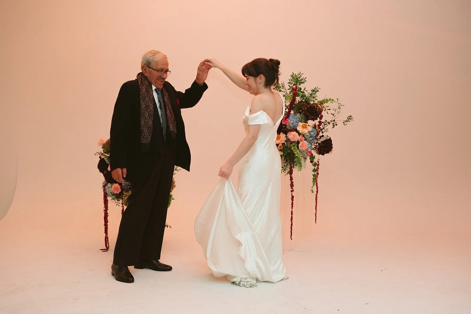 A bride dancing with an older man during a wedding ceremony with floral arrangements in the background. marigolds florals nyc florist wedding florals atmosfera wedding intimate wedding