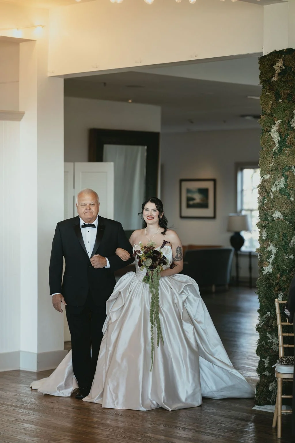 A bride in a white wedding gown walking down the aisle with her father, who is wearing a black tuxedo. marigolds florals nyc florist wedding florals