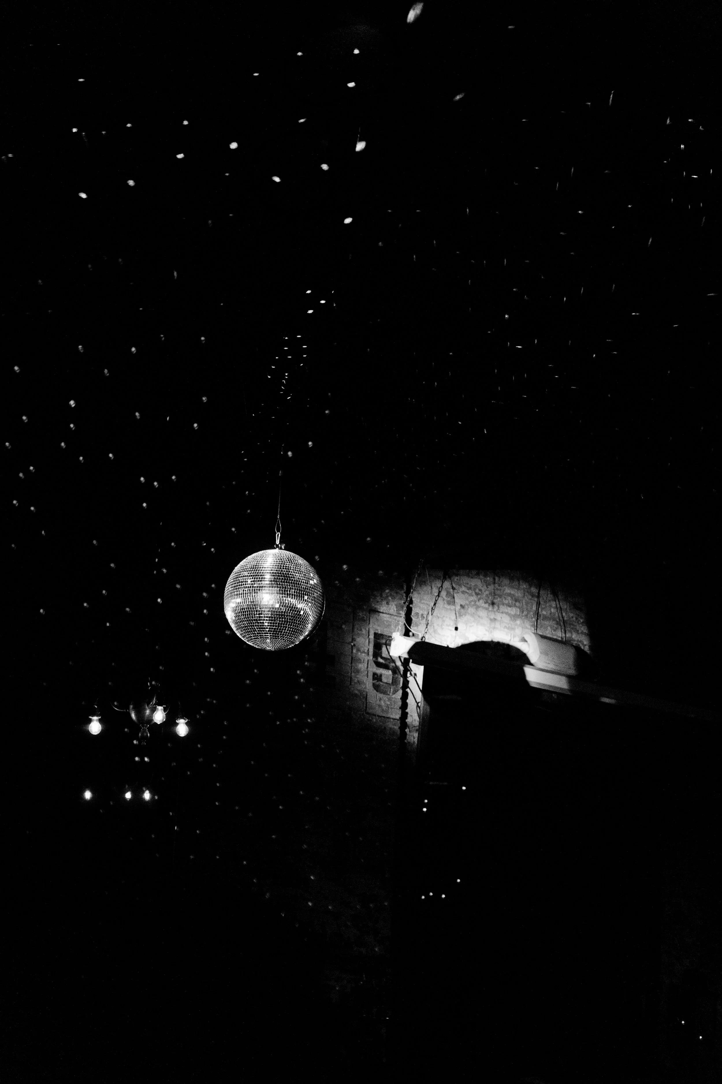 A black and white photo of a ceiling with small string lights and two disco balls hanging from it. marigolds florals nyc florist wedding florals houston hall nyc bar wedding