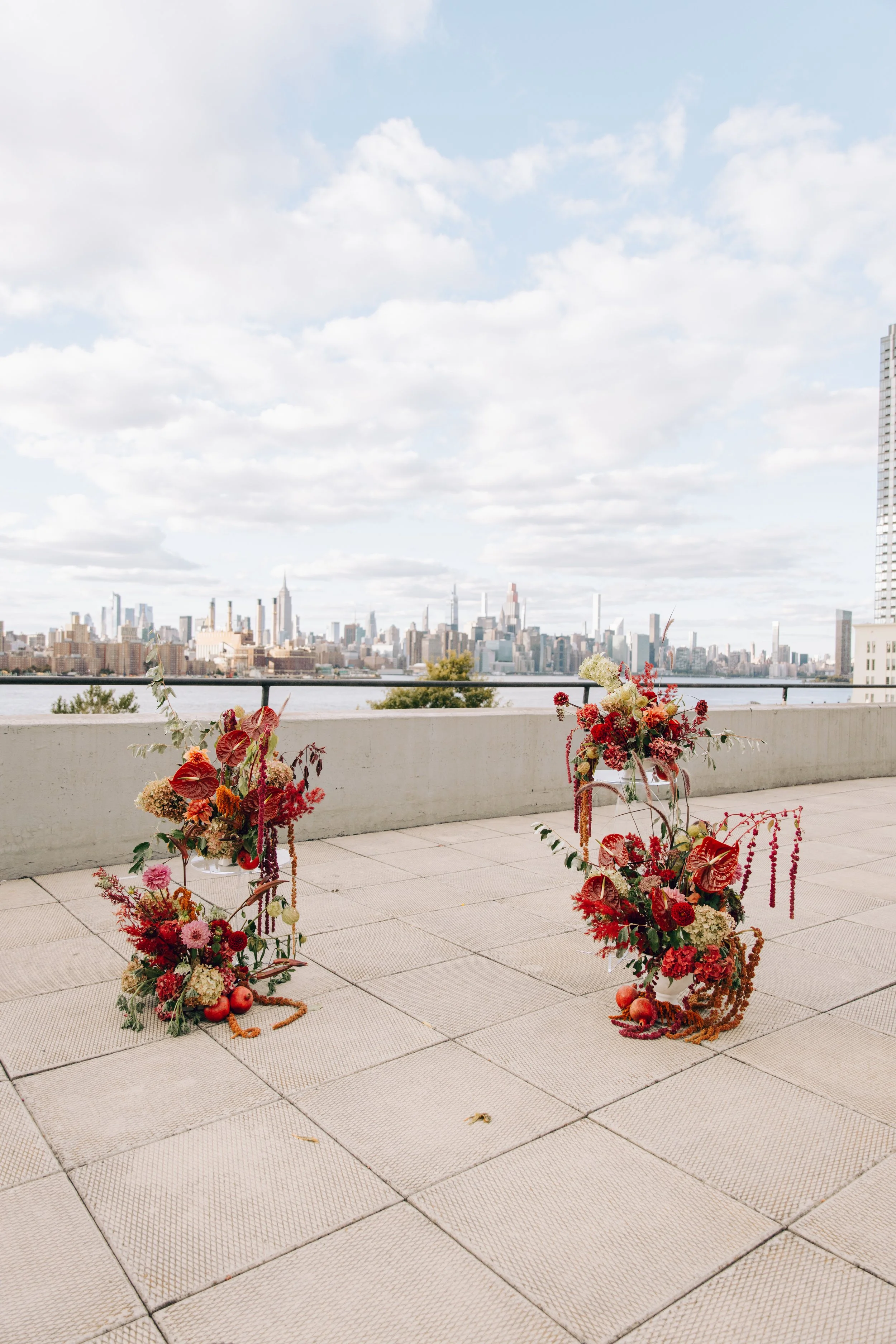 Colorful flower arrangements on a terrace overlooking the New York City skyline with a cloudy sky. marigolds florals nyc florist wedding florals the w loft wedding pedestal wedding ceremony anthurium 