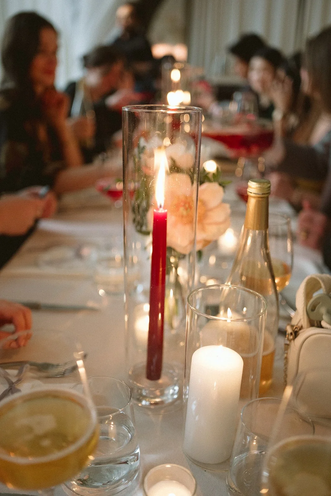 A dinner table with lit candles and a floral centerpiece, surrounded by people, during an evening gathering or celebration. marigolds florals nyc florist wedding florals atmosfera wedding