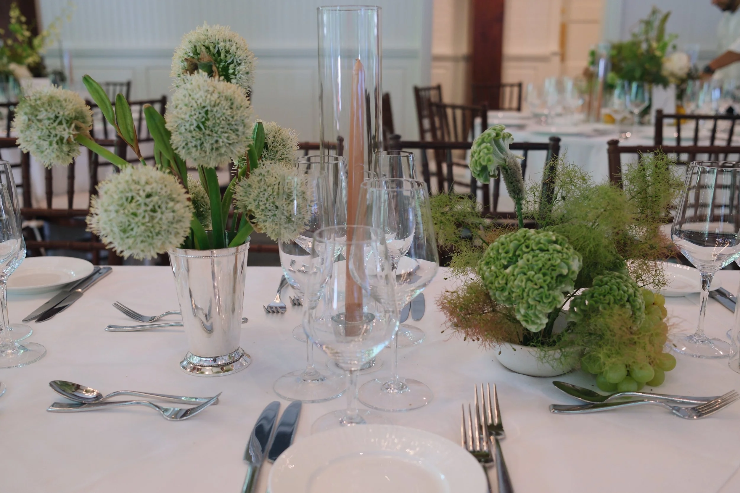 Elegant banquet table with floral centerpieces, wine glasses, silverware, and white plates, set for a formal event in a spacious, decorated room. marigolds florals nyc florist wedding florals central park boathouse wedding