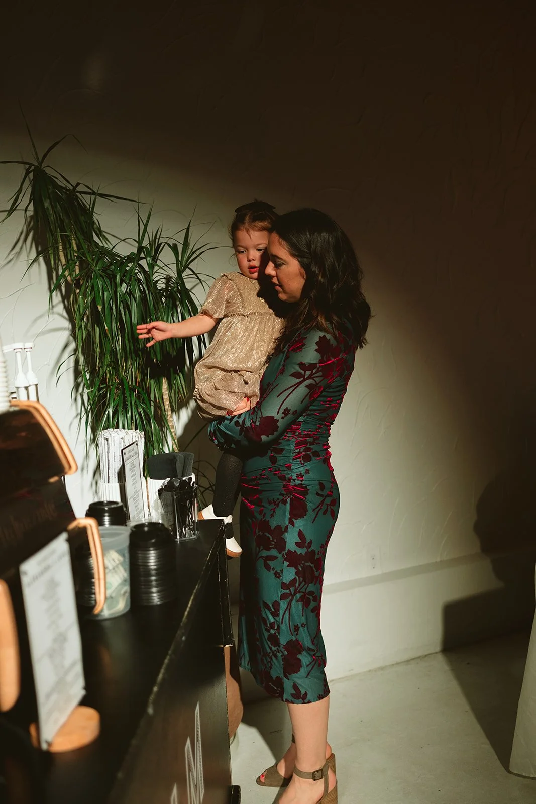 A woman holding a young girl at a counter in a dimly lit indoor setting. marigolds florals nyc florist wedding florals atmosfera wedding intimate wedding