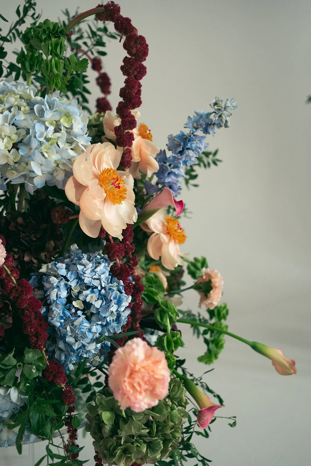 A close-up of a colorful flower arrangement featuring pink carnations, blue hydrangeas, purple veronica, and green leaves. marigolds florals nyc florist wedding florals atmosfera wedding