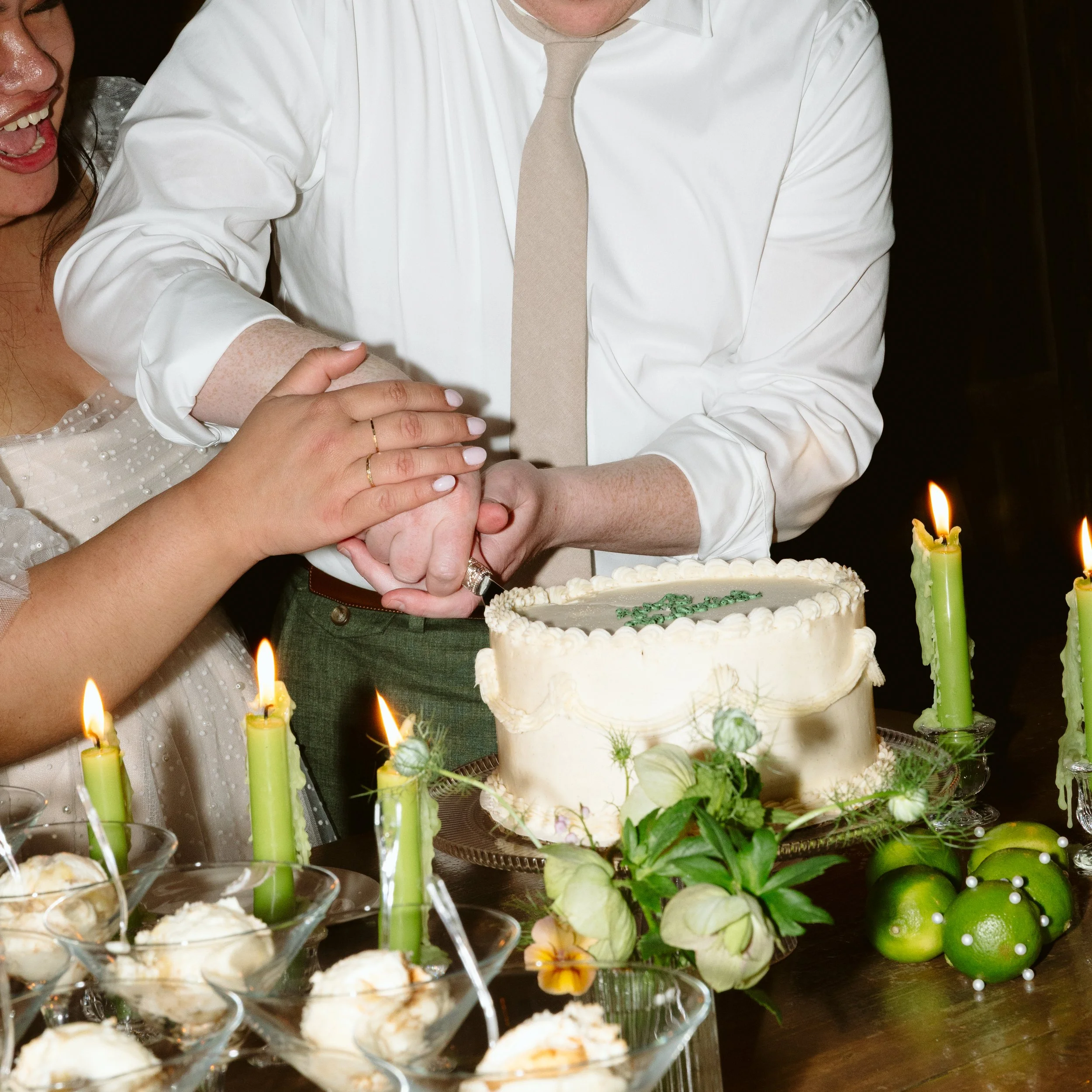 Close-up of a wedding celebration with a wedding cake, green candles, and small glasses of dessert, surrounded by floral decorations. marigolds florals nyc florist wedding florals houston hall nyc bar wedding