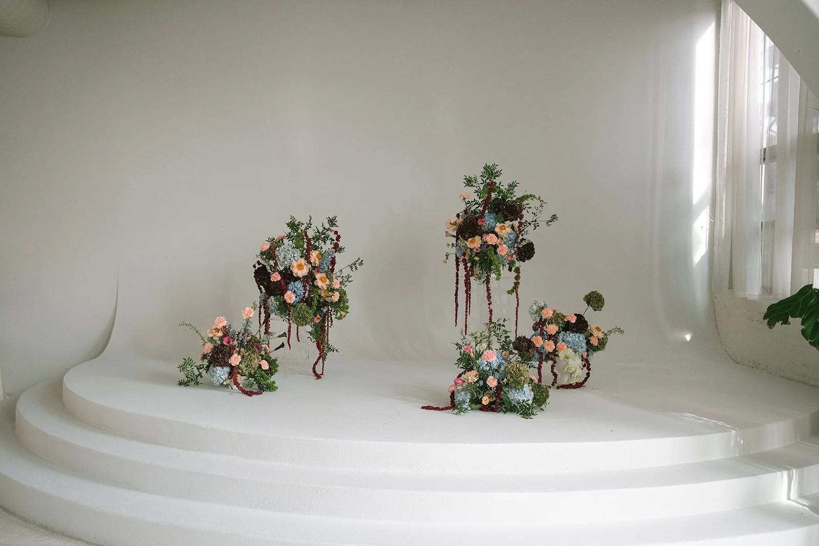 Elegant flower arrangements on white curved steps with natural light from window on the right. marigolds florals nyc florist wedding florals atmosfera wedding