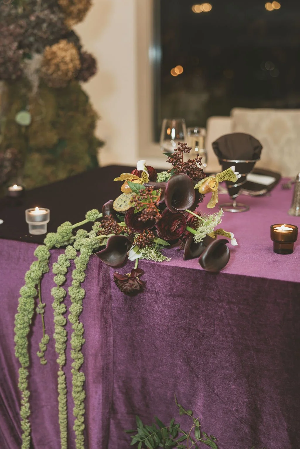Elegant dining table with purple tablecloth, floral centerpiece, black candles, and glassware, set in a sophisticated venue.  marigolds florals nyc florist wedding florals the garrison