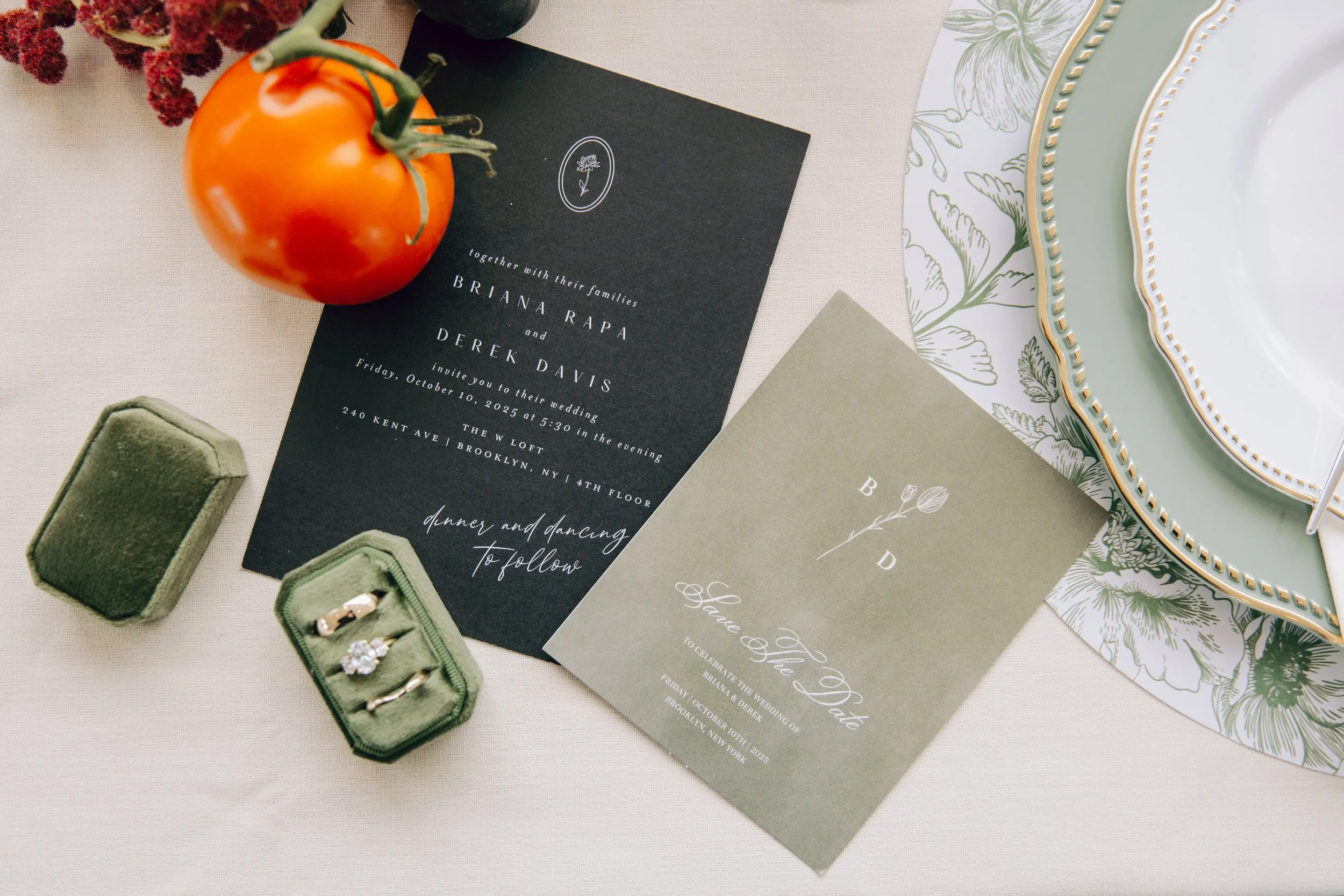 Wedding invitation cards on a table with a vintage plate, a tomato, jewelry boxes, and a decorative cloth. marigolds florals nyc florist wedding florals the w loft wedding pedestal wedding ceremony anthurium 