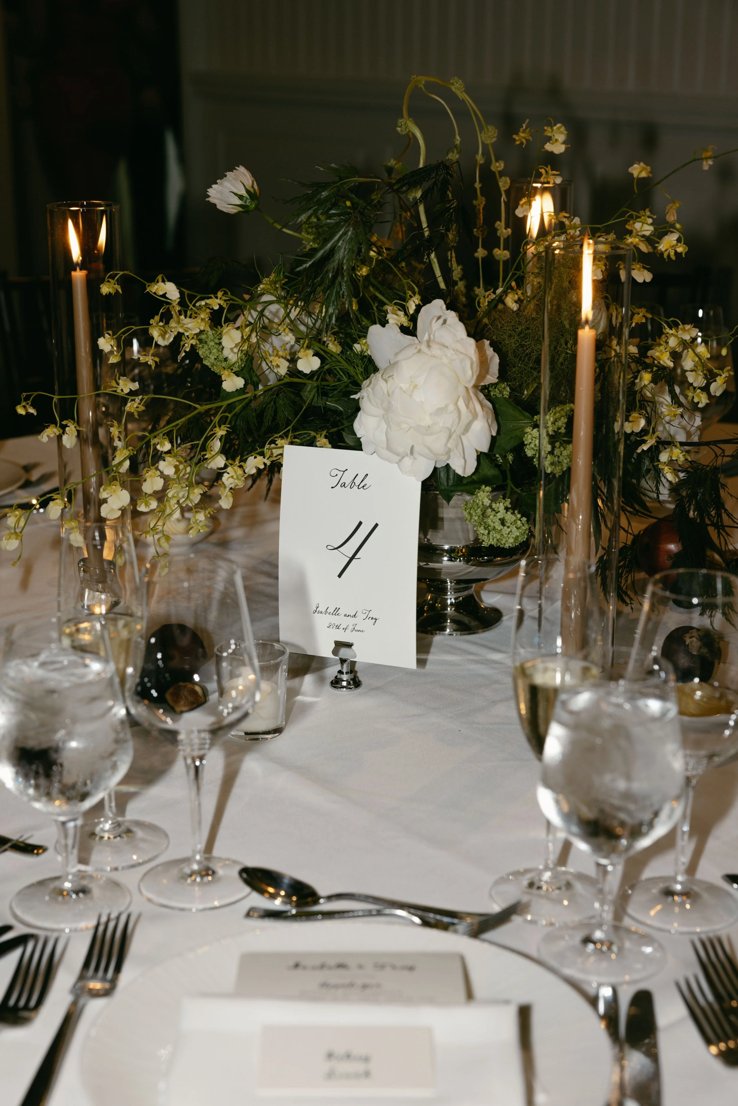 Elegant table arrangement with white flowers, candles, glassware, and place cards, likely for a formal event or wedding reception. marigolds florals nyc florist wedding florals central park boathouse wedding