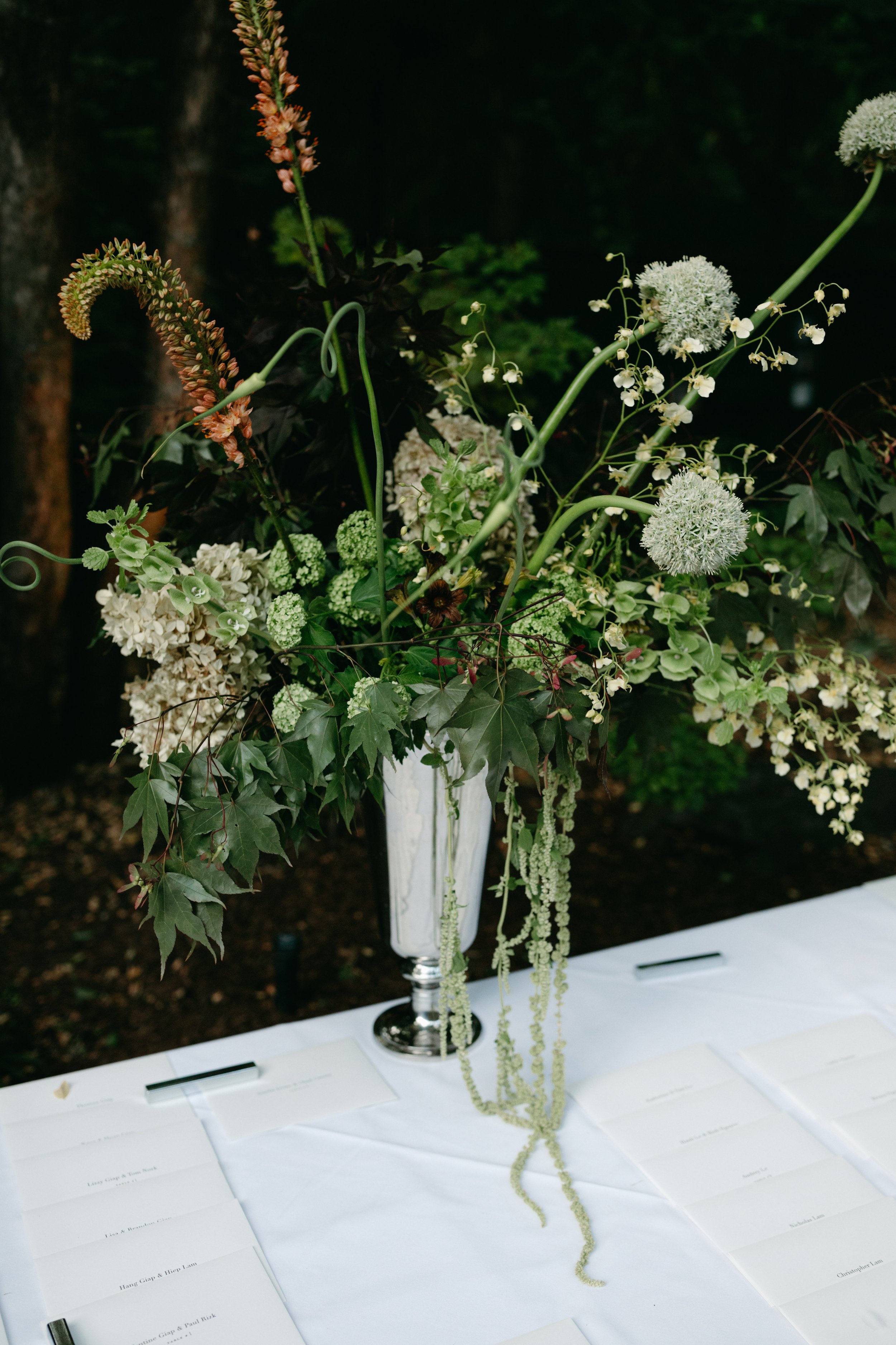 Floral centerpiece with white flowers, greenery, and hanging green beads on a white table.  marigolds florals nyc florist wedding florals central park boathouse wedding