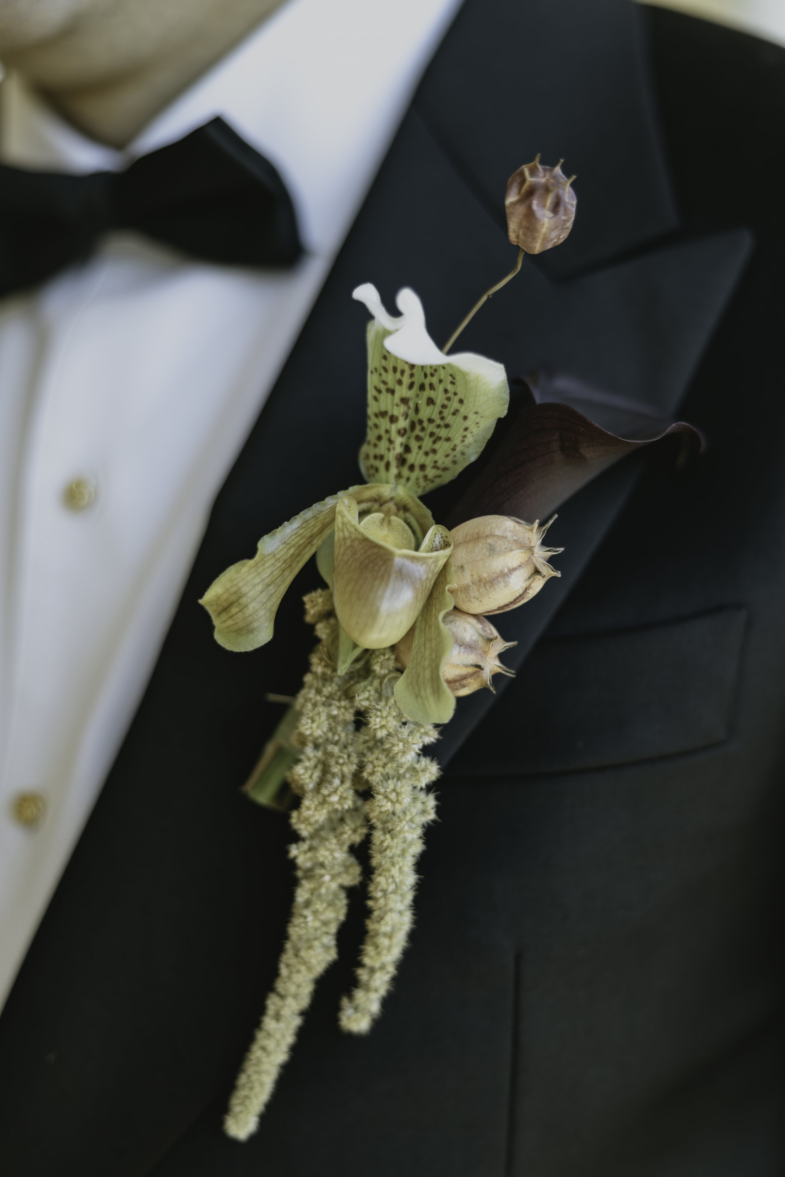 A boutonniere with dried flowers worn on a black tuxedo jacket.  marigolds florals nyc florist wedding florals the garrison