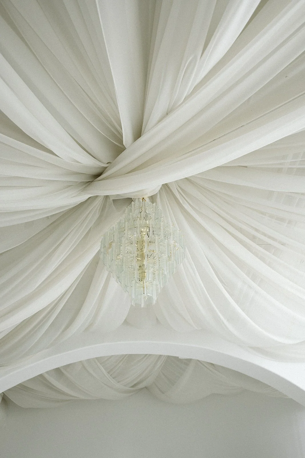 Ceiling draped with white fabric and a chandelier hanging in the center. marigolds florals nyc florist wedding florals atmosfera wedding