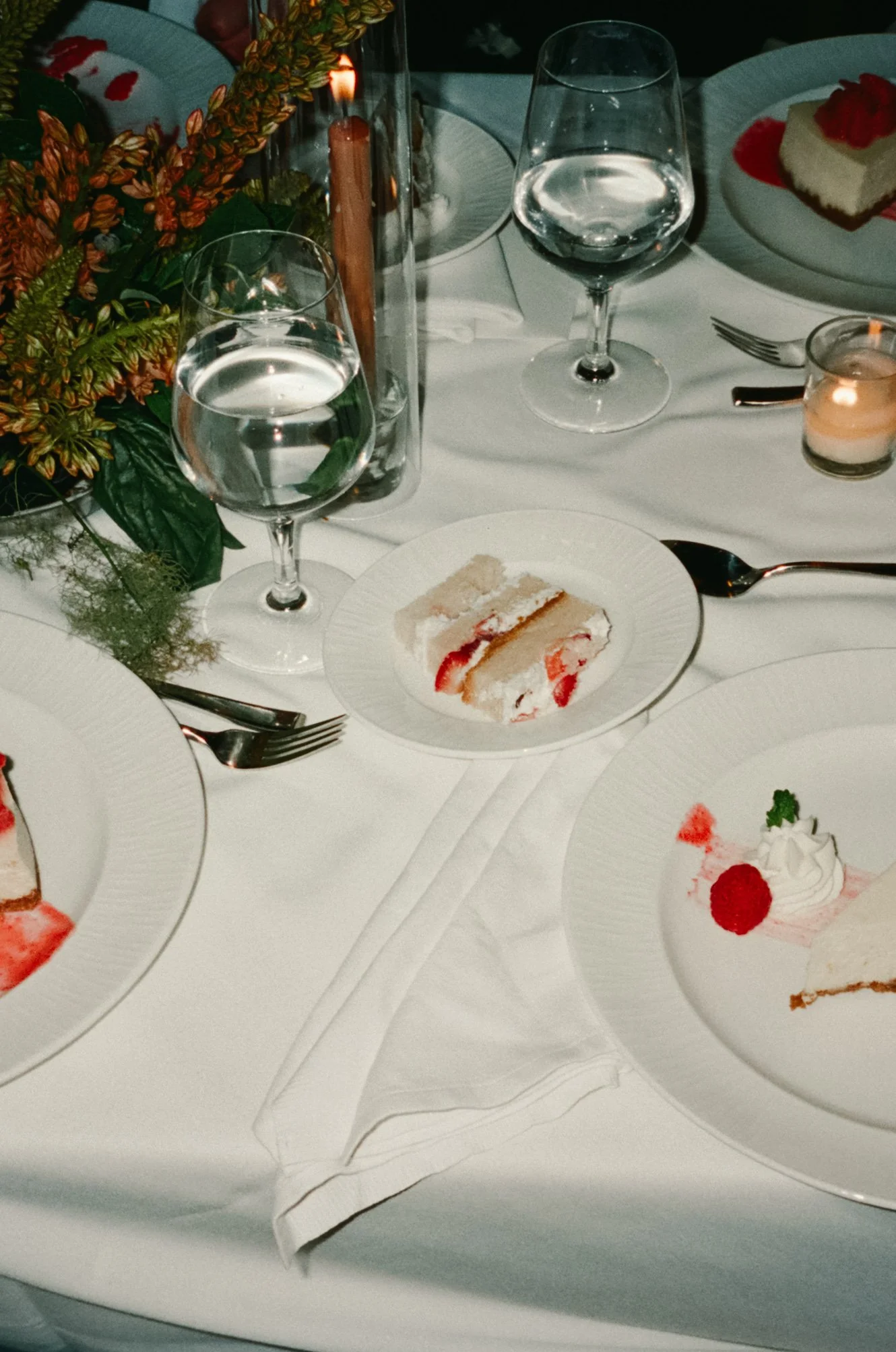 A table set with plates, glasses of water, a plate with dessert, and a floral centerpiece at a festive dinner event. marigolds florals nyc florist wedding florals central park boathouse wedding