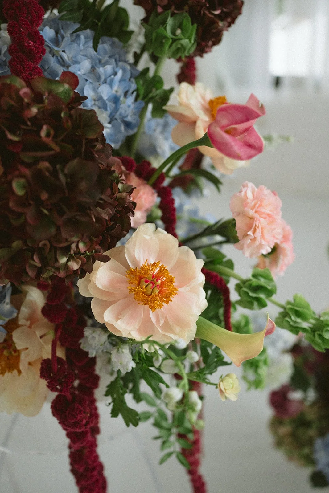A close-up of a mixed bouquet of flowers including pink peonies, blue hydrangeas, pale pink or peach roses, burgundy astilbes, and green foliage. marigolds florals nyc florist wedding florals atmosfera wedding
