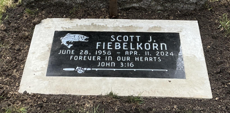 Gravestone for Scott J. Flbelkorn, born June 28, 1958, died April 11, 2024, with a fish graphic, inscribed with 'Forever in our hearts' and a reference to John 3:16.