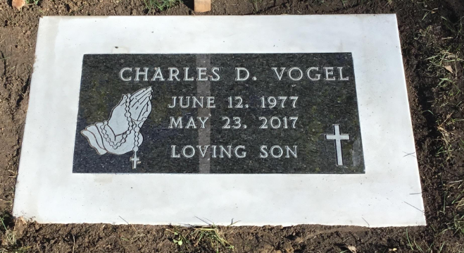 Gravestone for Charles D. Vogel with his birth and death dates, prayer hands and a cross engraved on it.