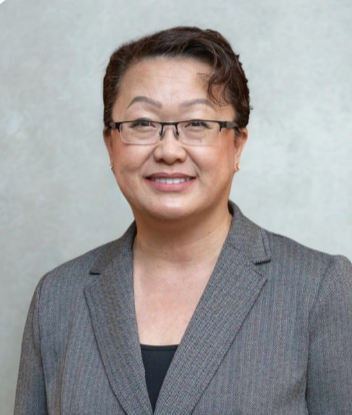 Professional woman wearing glasses and a gray blazer, smiling against a neutral background.