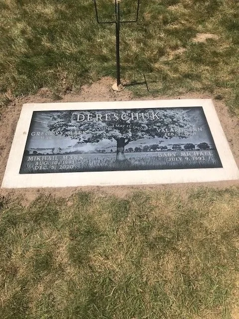 Gravestone with a tree engraved in the center and the name 'DERECHUK' at the top, including birth and death dates, and other names and dates at the bottom.