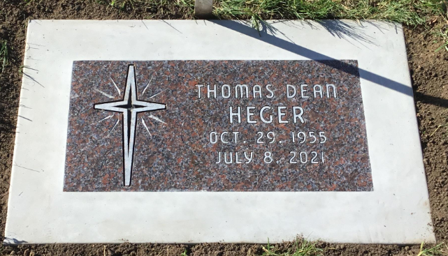 Gravestone for Thomas Dean Heger with a cross symbol, displaying his birth date October 29, 1955, and death date July 8, 2021, surrounded by grass and soil.