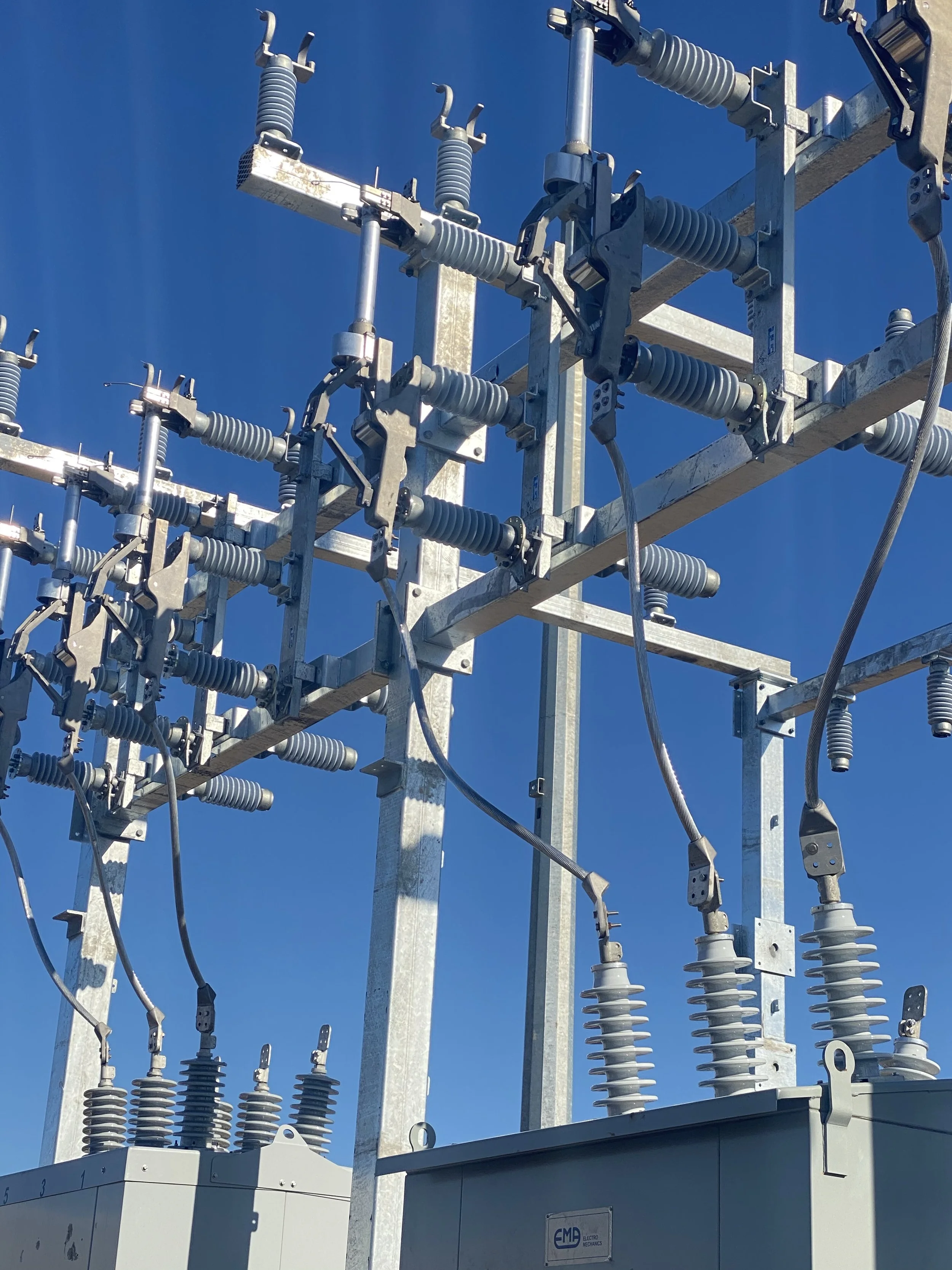Close-up view of electrical power transmission equipment with insulators and conductors against a clear blue sky.