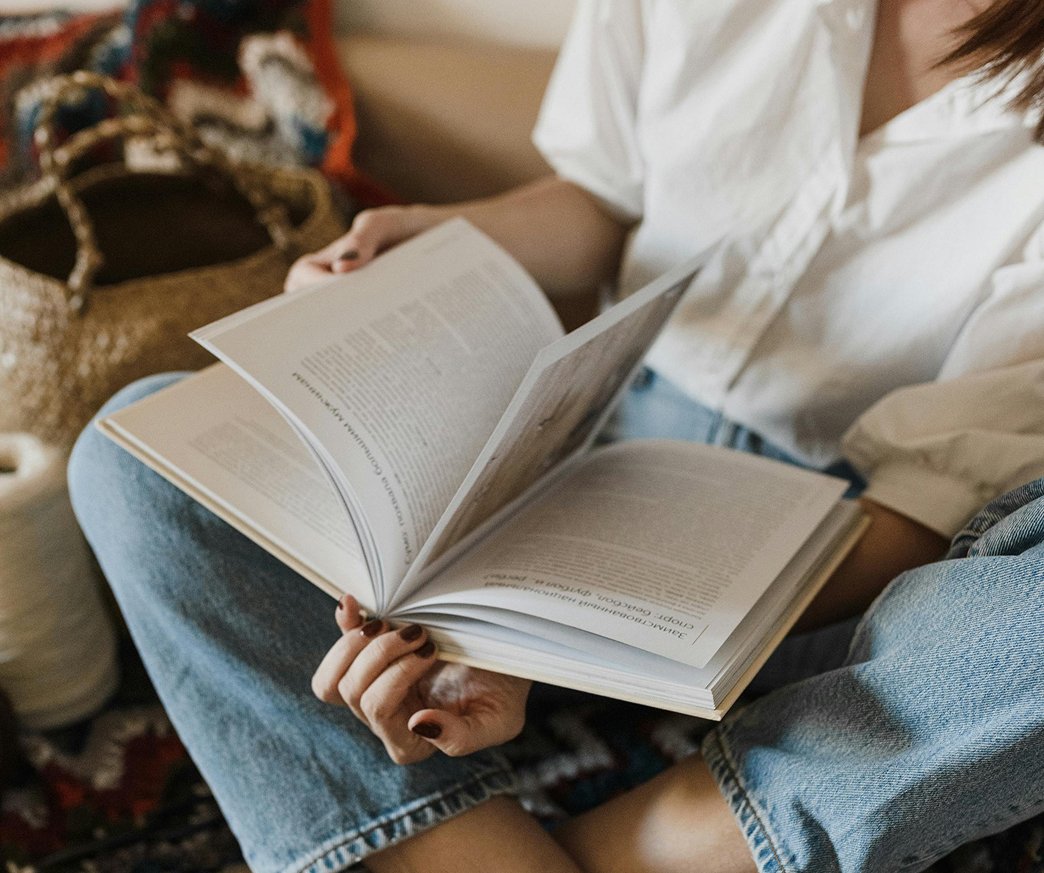 Person sitting on a colorful rug, reading a magazine or book, wearing a white shirt and blue jeans.