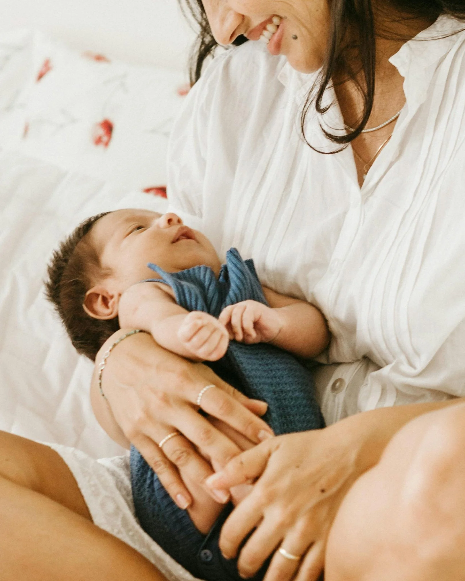 A woman holding a newborn baby in her arms, looking at the baby with a smile.