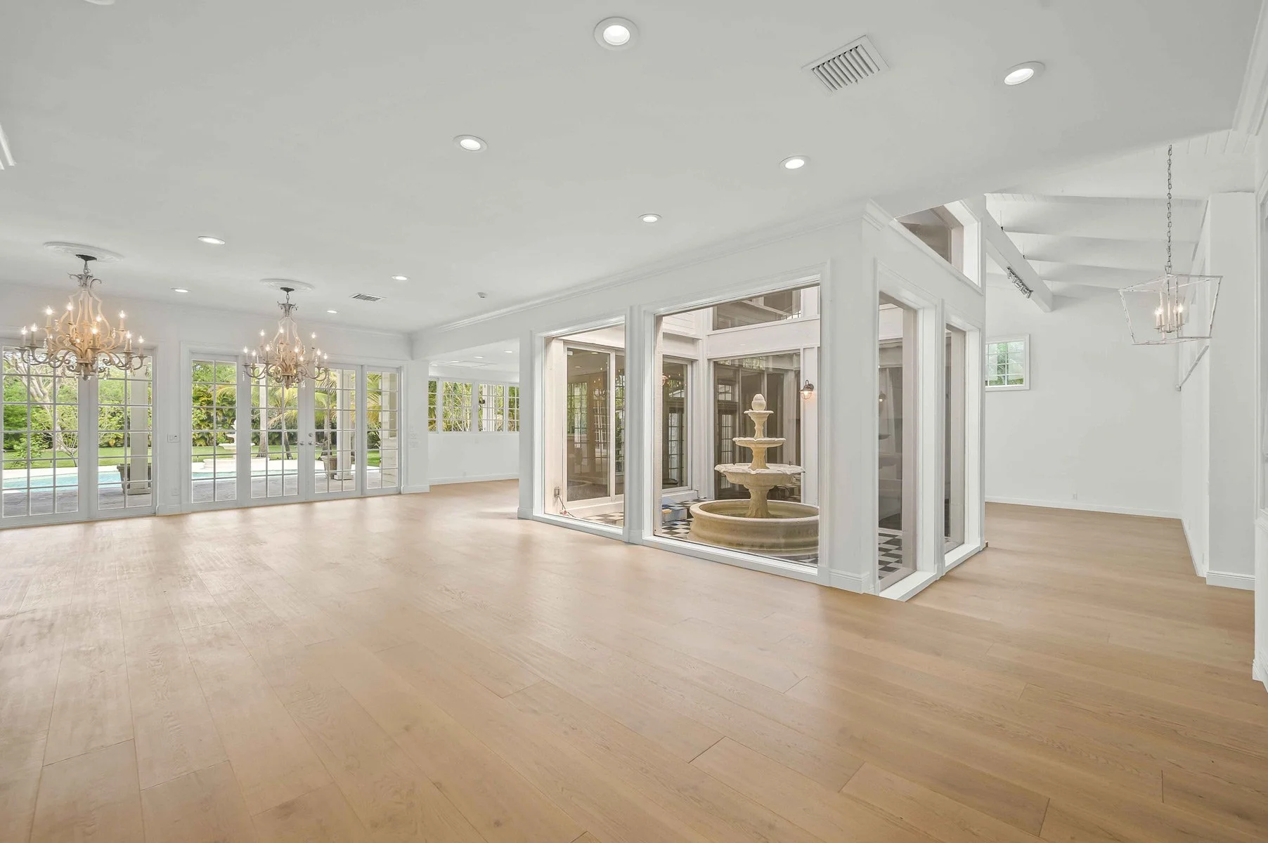 Spacious, bright living room with hardwood floors, large windows, and a central fountain in a glass-enclosed area.