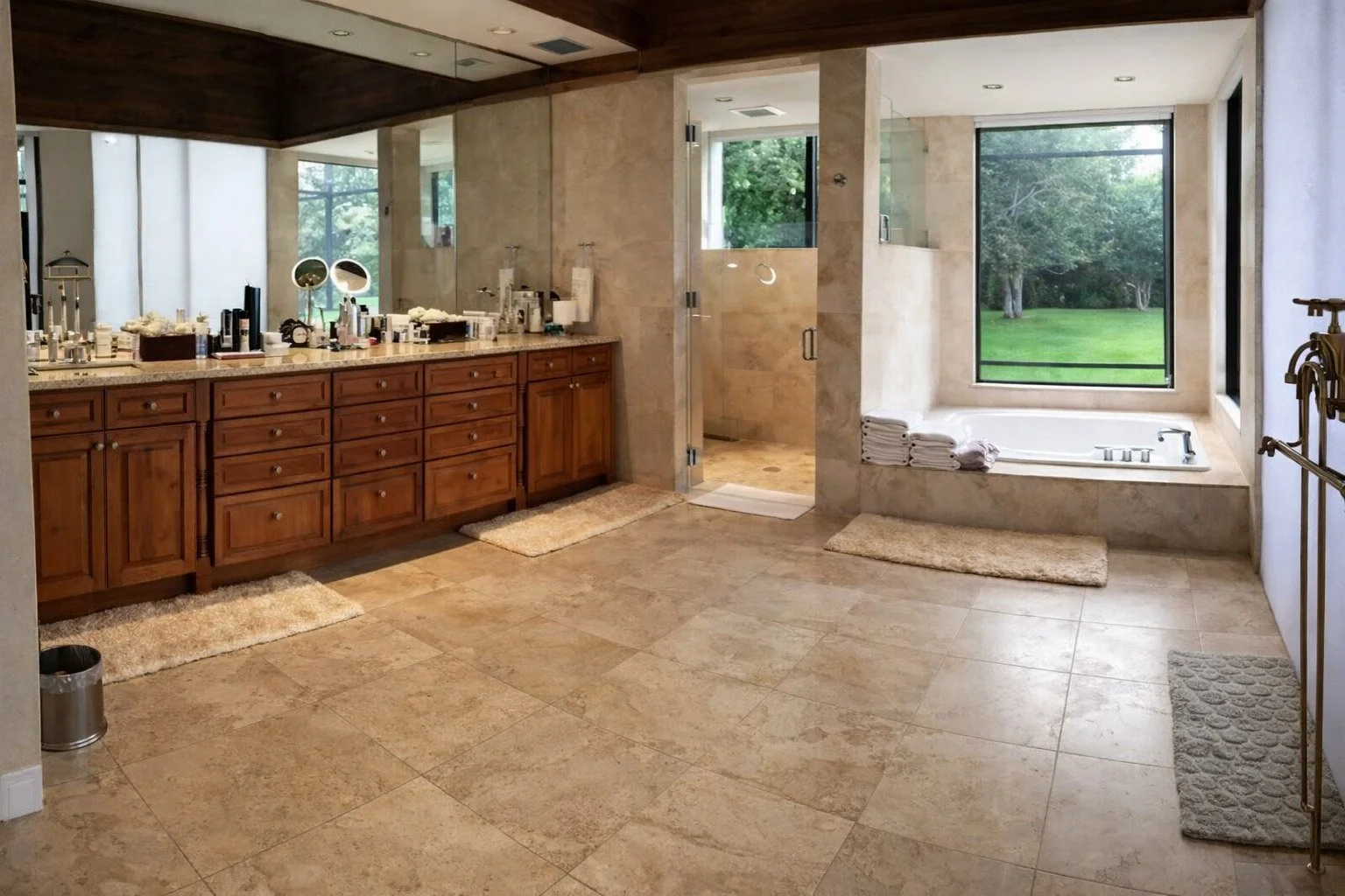 A spacious bathroom with a vanity area, a shower, a bathtub next to a large window with green outdoor view, and various toiletries and towels.