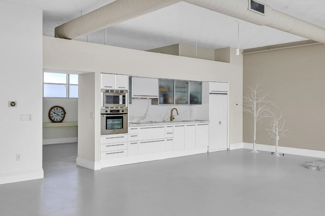 Modern kitchen with white cabinets, stainless steel appliances, a gold faucet, and minimalistic decor, including two white tree sculptures against a beige wall.