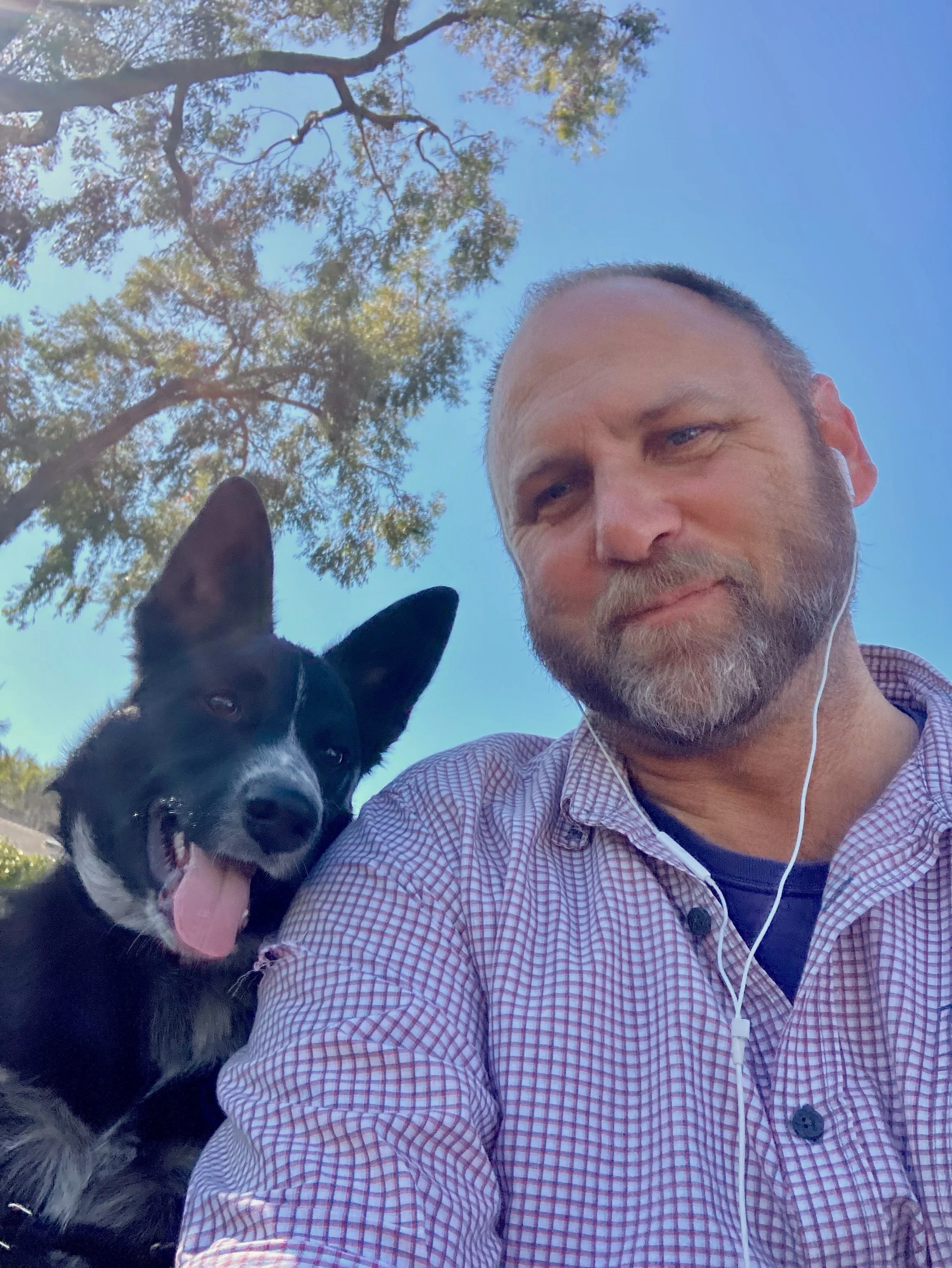 Dog Uncle Nate with black and white dog Australian Cattle Dog taking a selfie outdoors under a blue sky with trees.