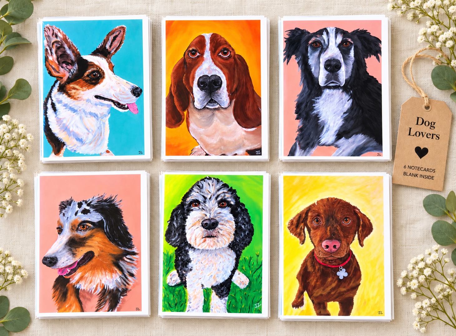 Six colorful illustrated dog portraits arranged on a beige surface, surrounded by white flowers and green leaves, with a tag that says 'Dog Lovers' and indicates 6 notecards inside.