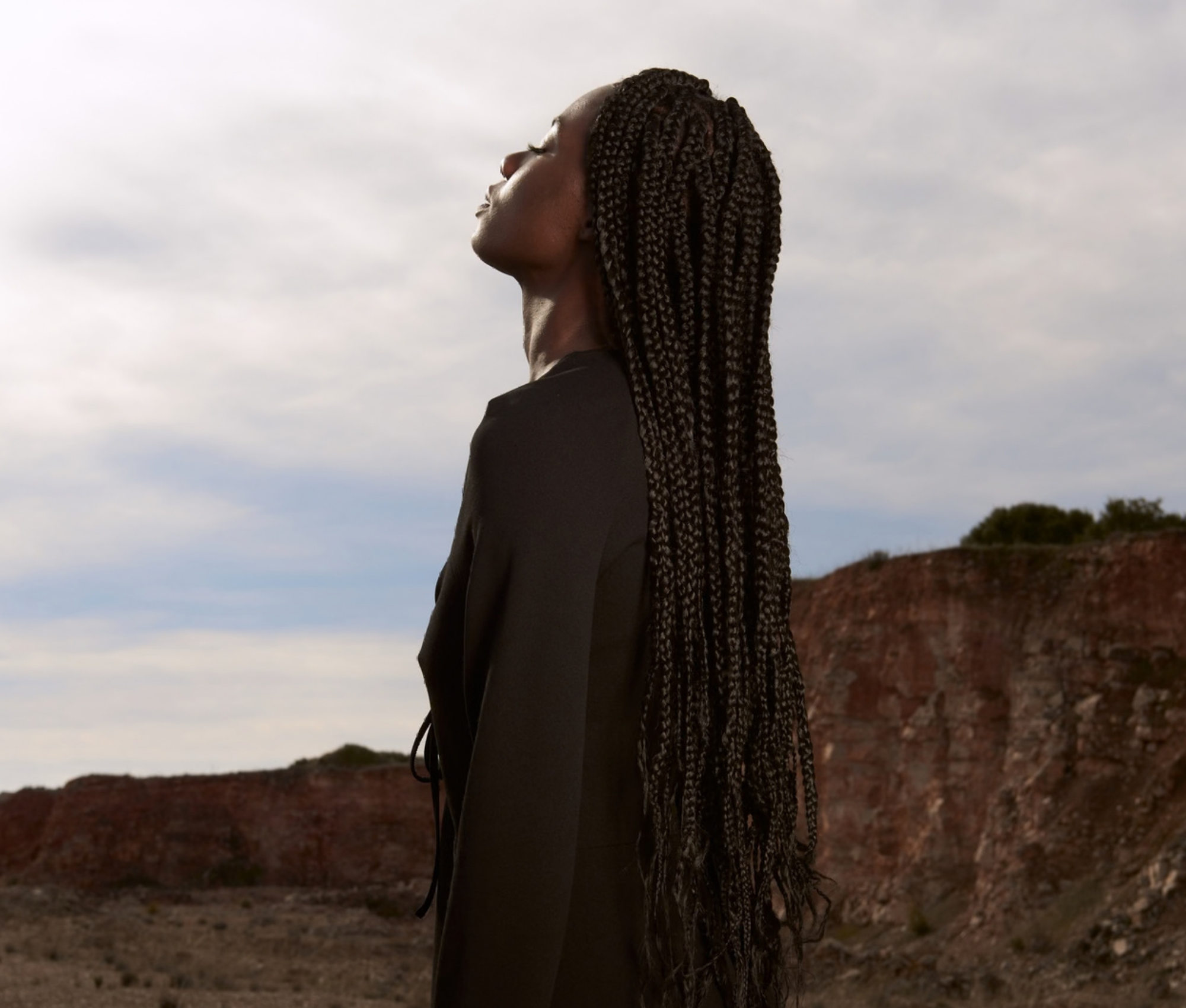 Black woman with long box braids standing outdoors with head tilted back, representing self-alignment and healing through affirming therapy at Say More Therapy