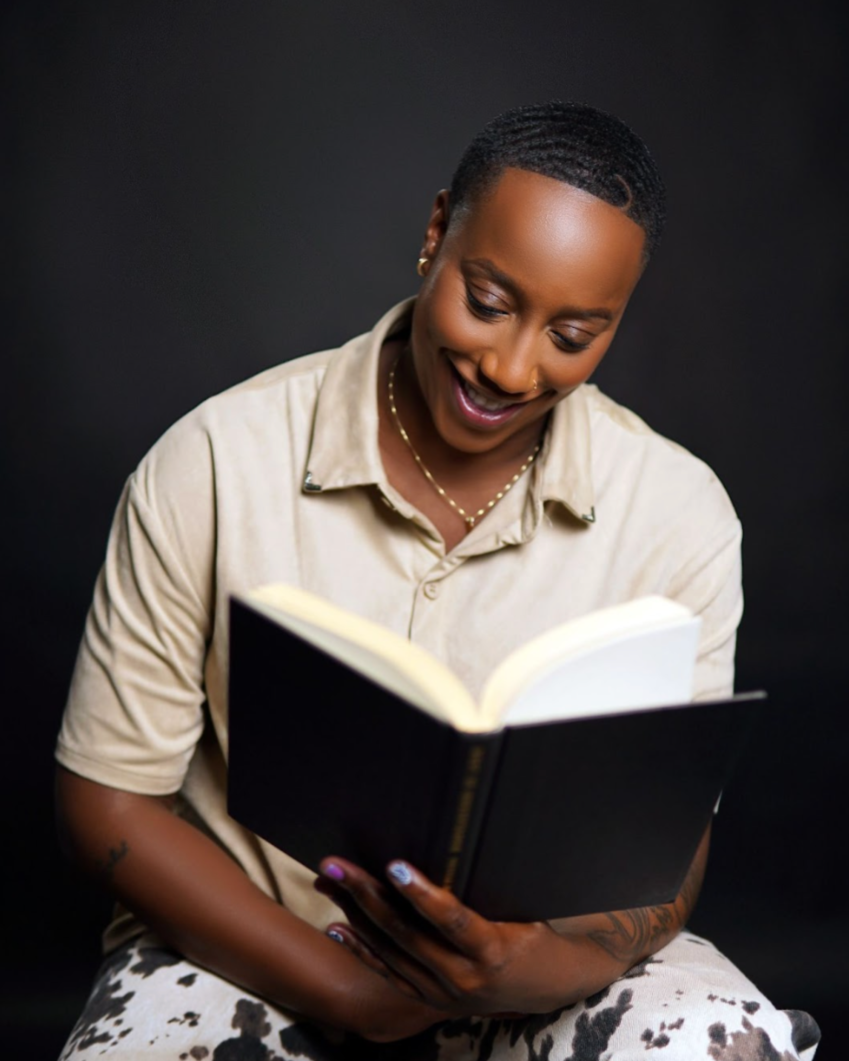 Say More Therapy based in Maryland. Therapist Ramelle Liverpool  with short hair reading a black-covered book against a dark background.