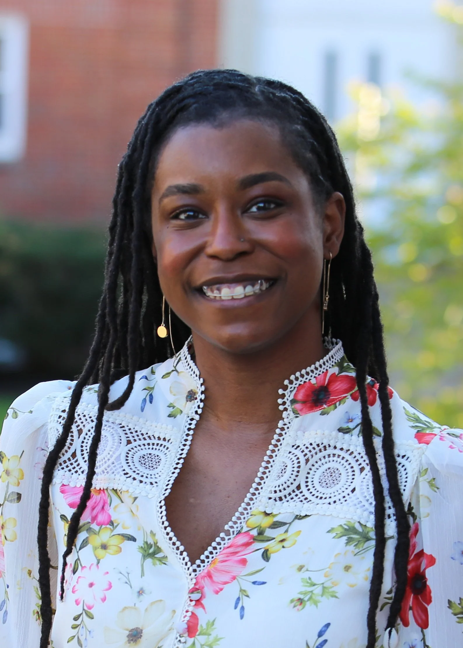 Alleanna Harris, a Black woman with locs, stands outside and smiles.