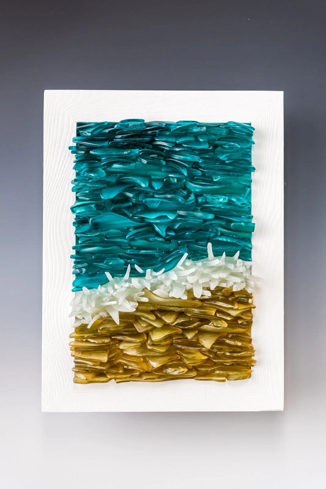 Abstract artwork with layered pieces in shades of blue, white, and beige, mounted on a white canvas.