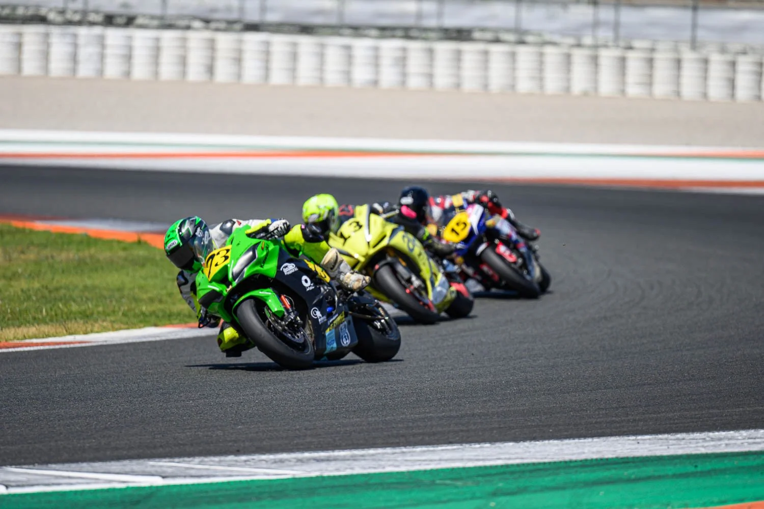 Tres motociclistas compitiendo en una carrera en una pista de carreras, inclinados mientras toman una curva.