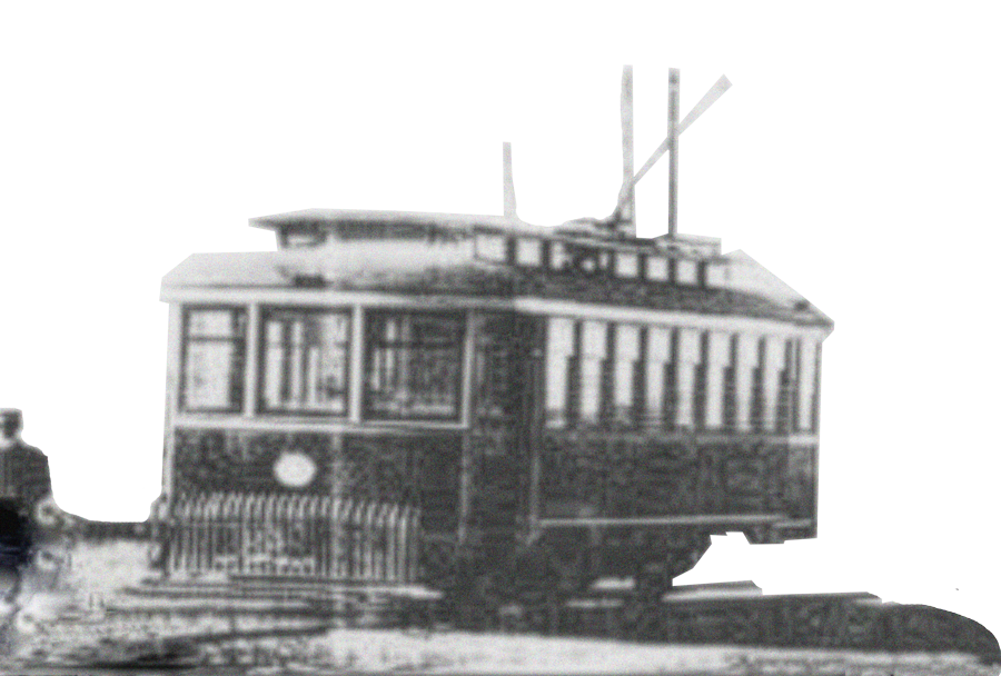 Black and white photo of an old trolley or streetcar with a person standing nearby.