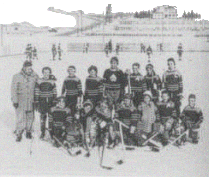 A group of children and adults posing on an outdoor ice skating rink, with some holding hockey sticks and wearing winter clothes.