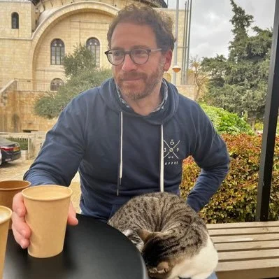Photo of professor Joel S. Baden with a coffee cup in his hand and a cat on his lap