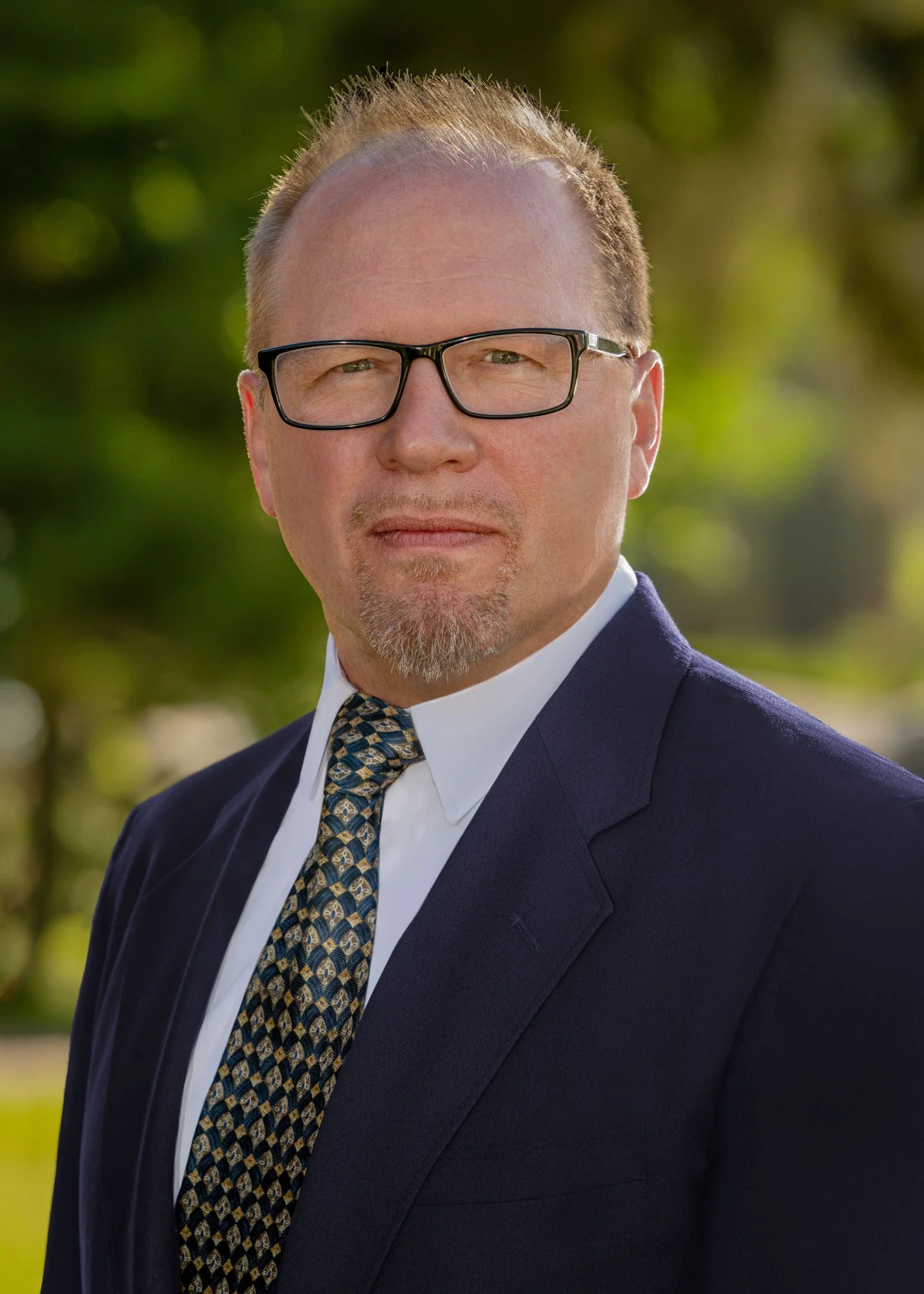 Headshot of Thomas Jay Oord with trees in the background. Tom is wearing a suite and tie.