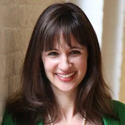Headshot of Meghan Henning in front of brick wall in a hallway.