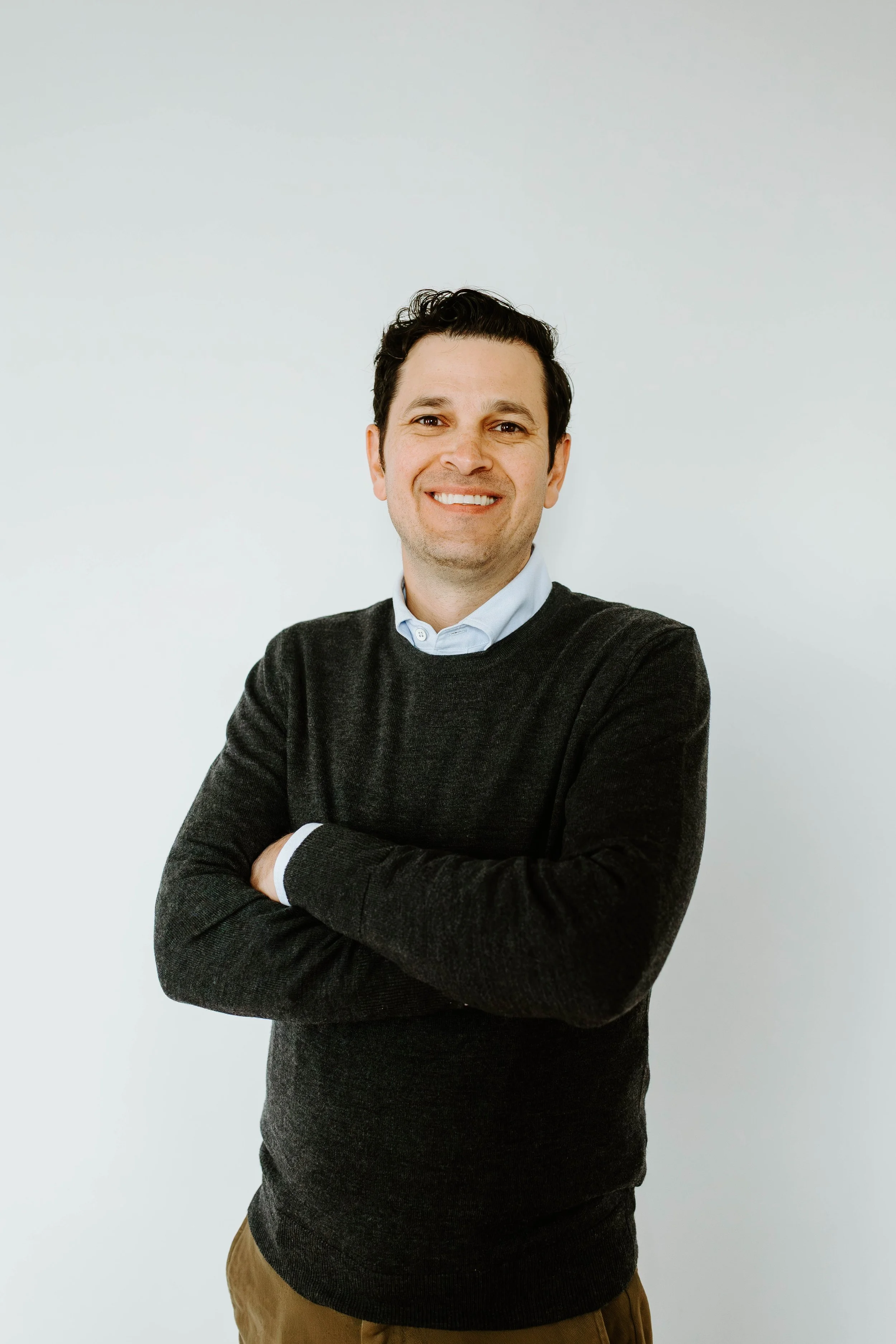 Headshot of Jared Byas smiling, with arms crossed, in front of a grayish white background