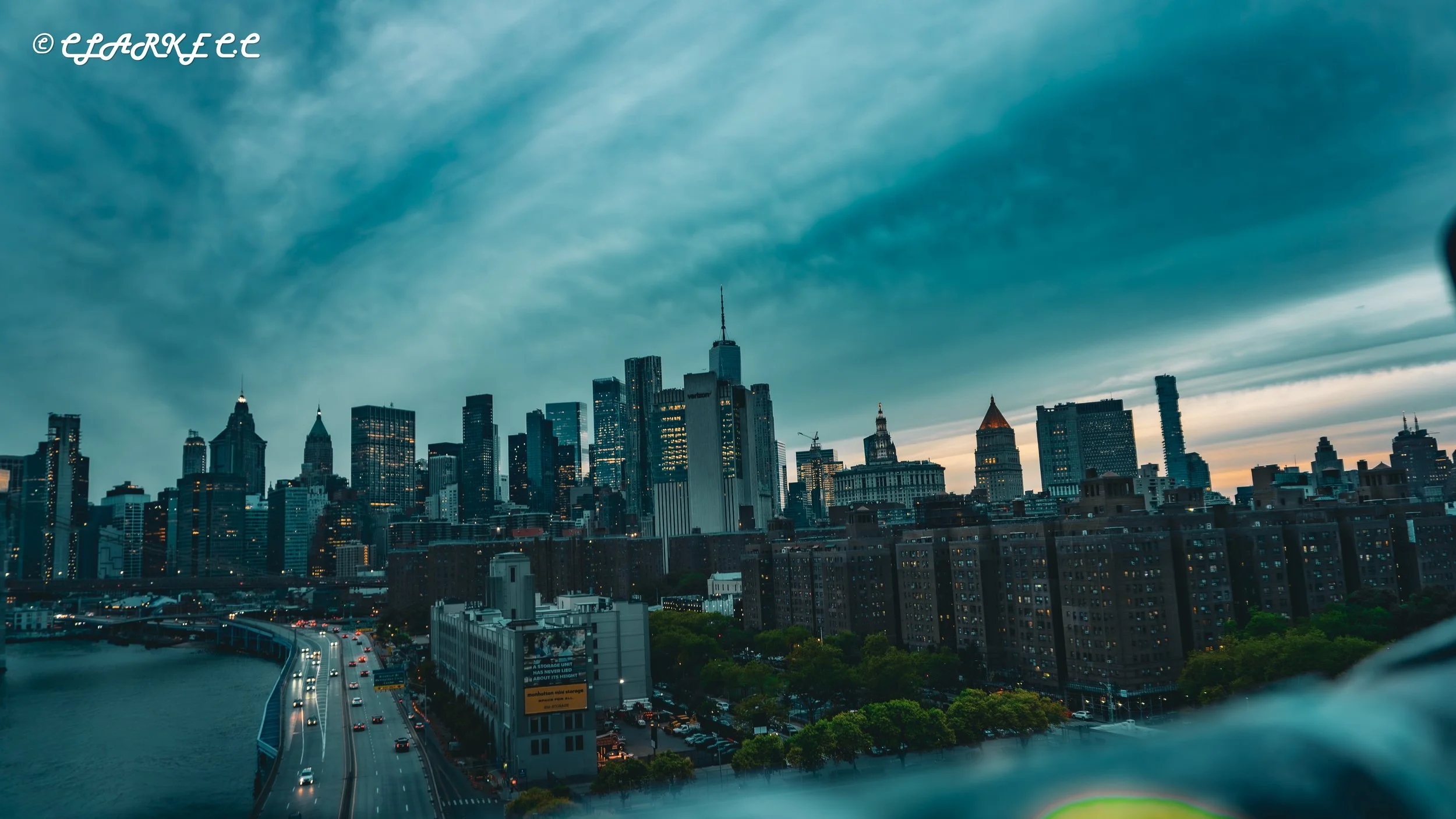 Skyline of New York City with tall skyscrapers and a river in the foreground during dusk.