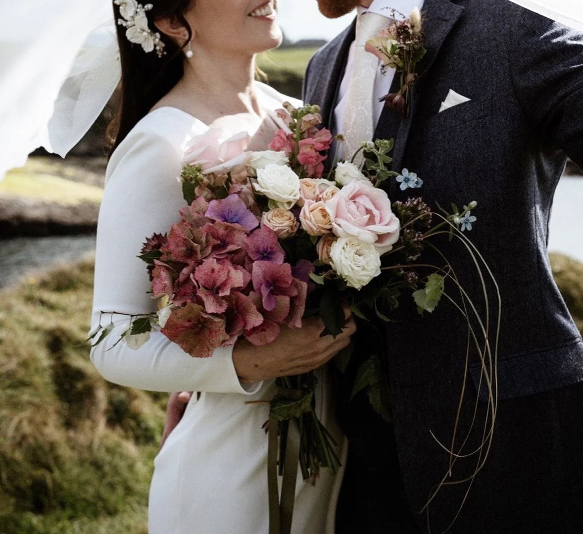 Bride and groom holding a bouquet of pink, white, and purple flowers during their wedding outdoors.