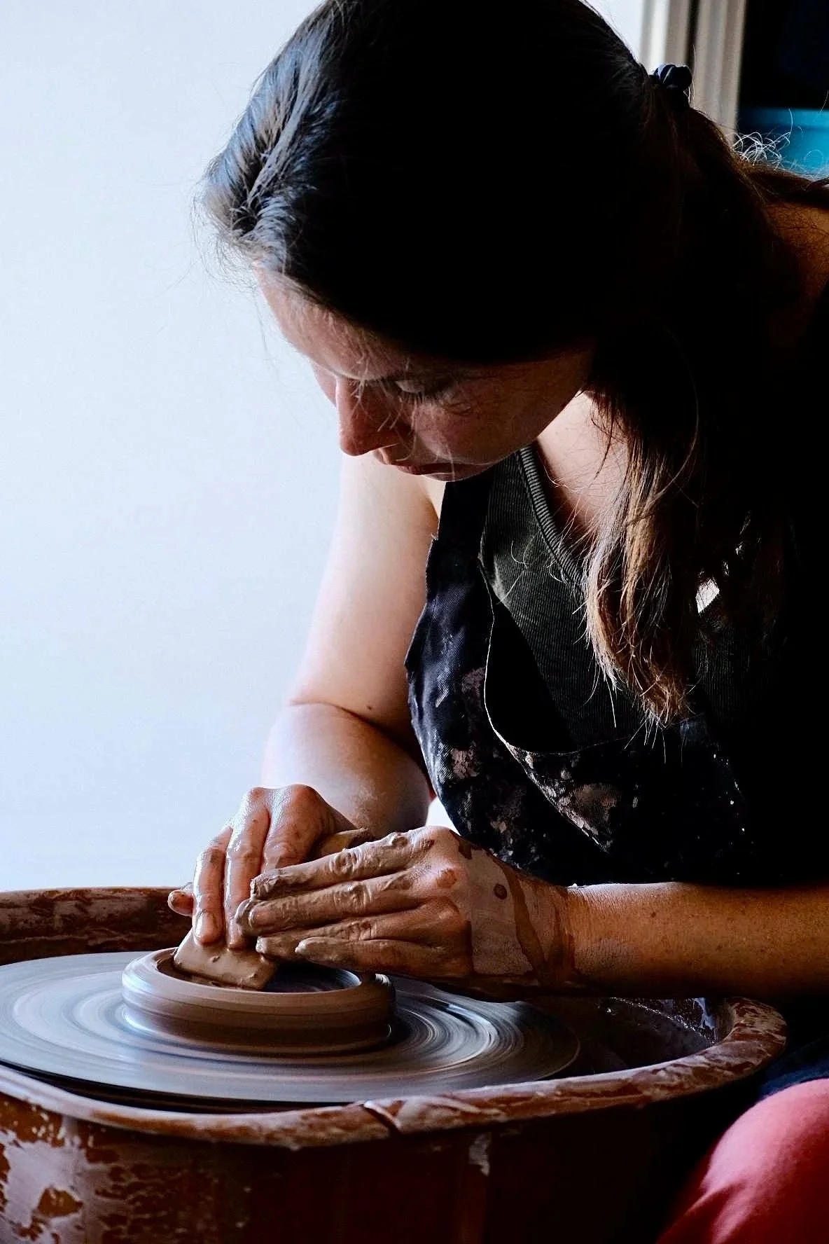 A woman pottery wheel throwing clay on a spinning wheel in a pottery studio.