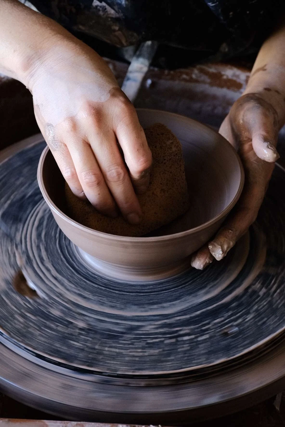 Hands shaping wet clay on a spinning pottery wheel.