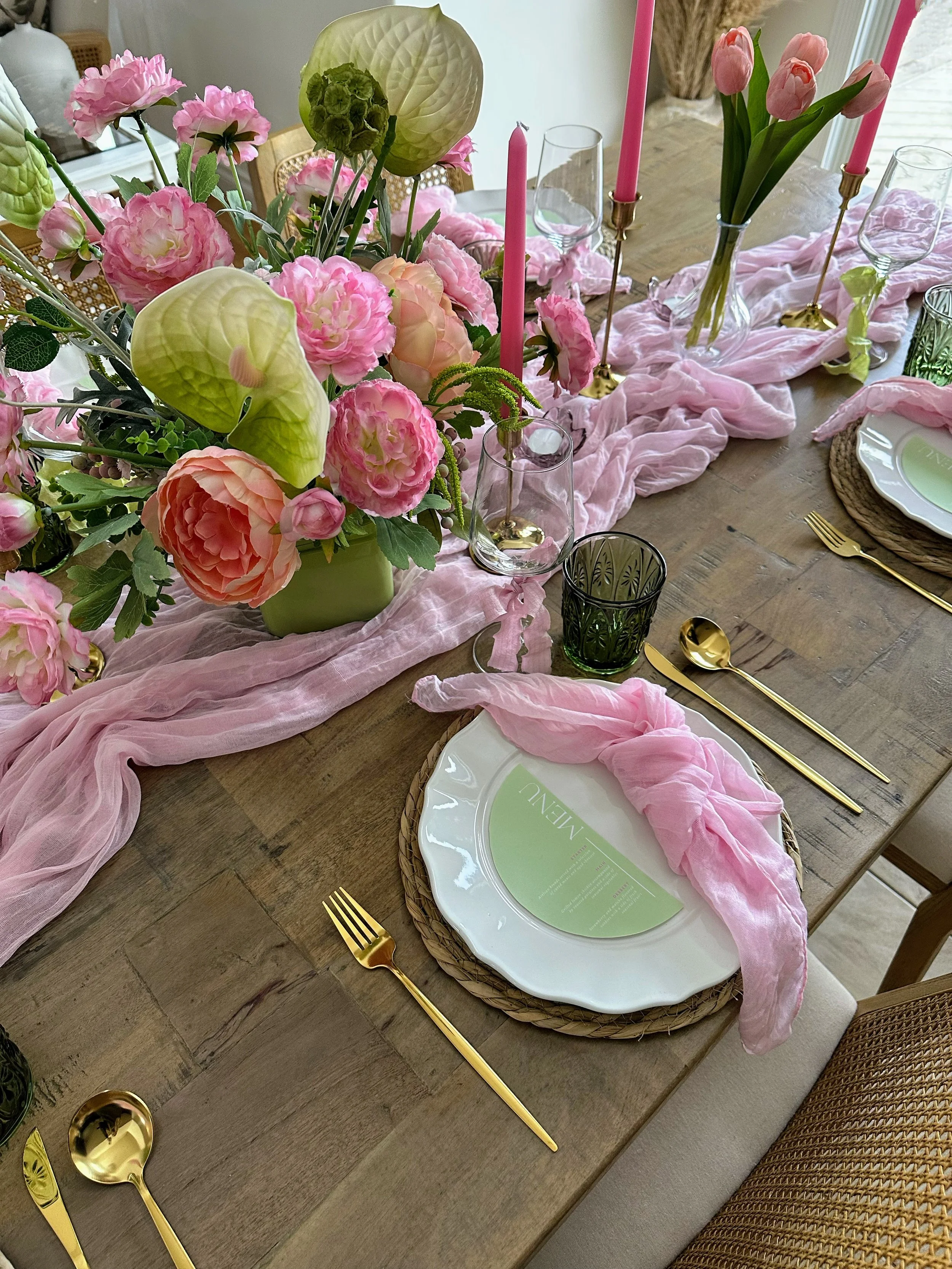 A beautifully decorated table with pink candles, floral centerpieces, matching pink plates, gold utensils, and a pale green tablecloth for a special occasion.