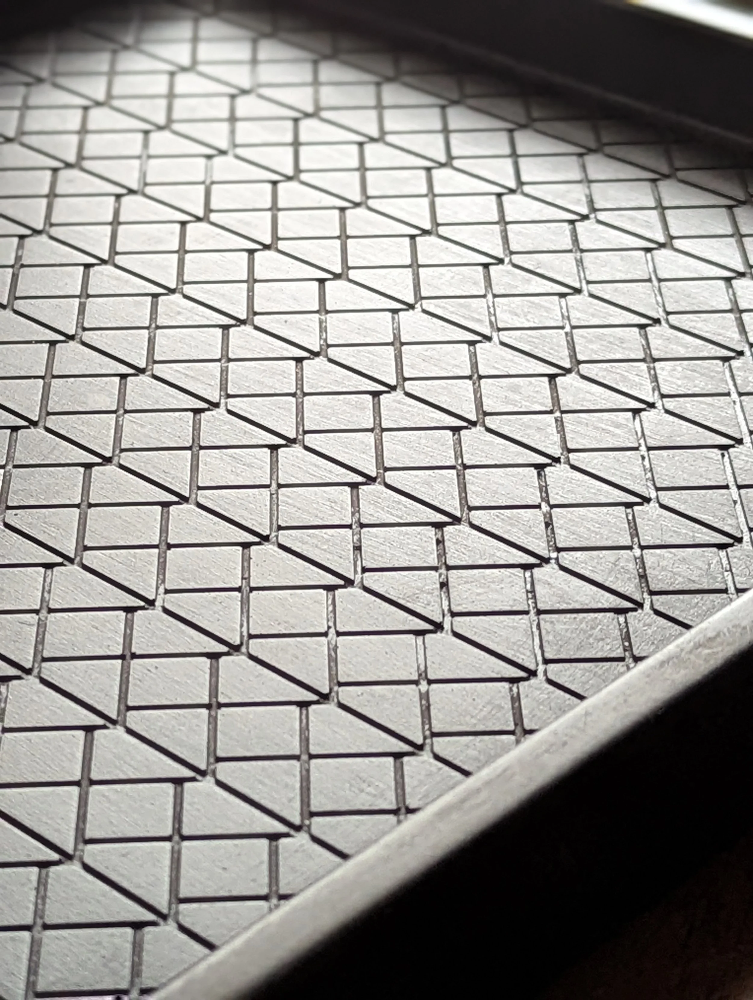 Close-up of a metal surface with a textured, geometric pattern of small, repeating diamonds and triangles.
