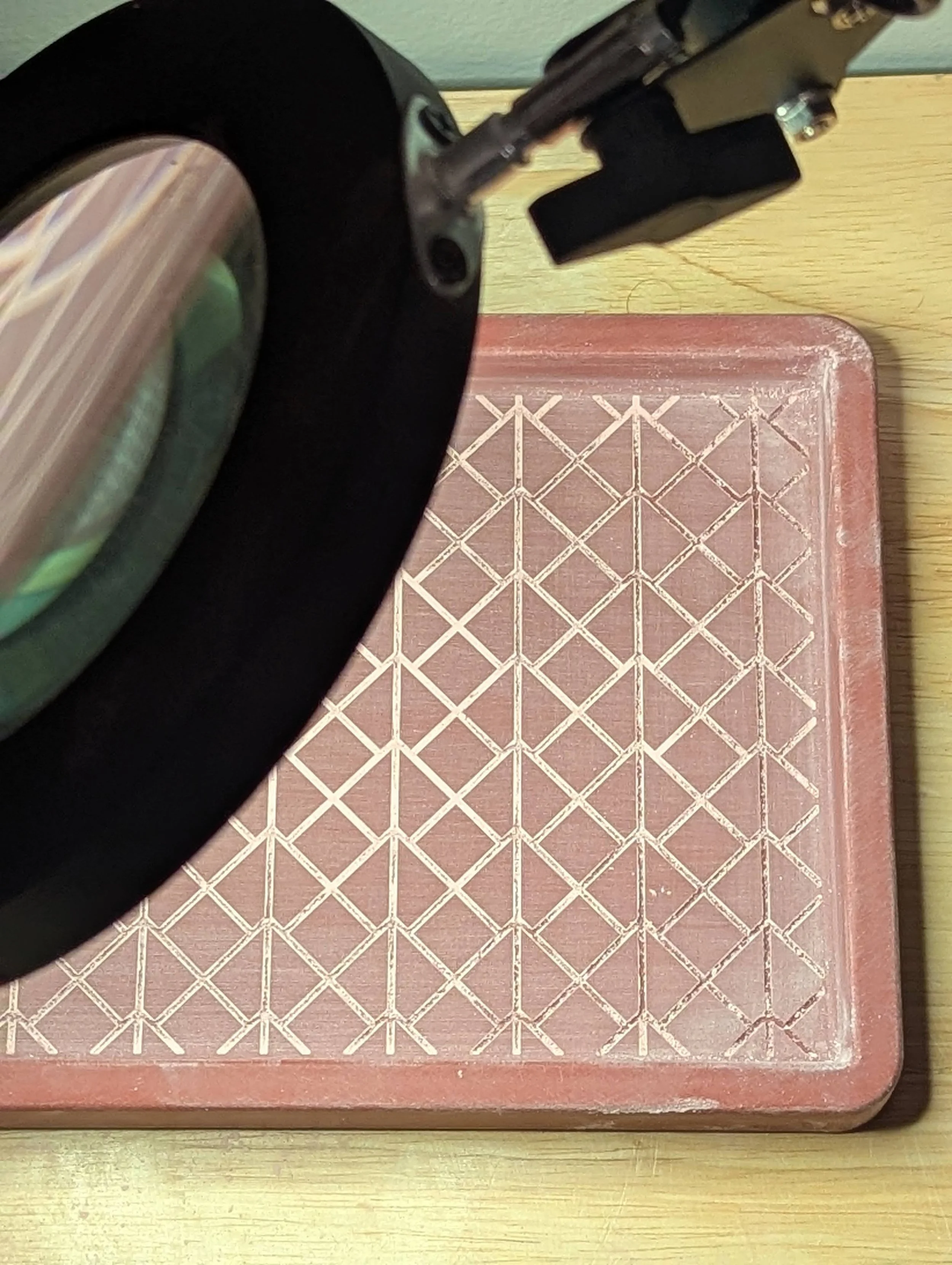 A close-up view of a microscope positioned over a pink ruler with grid lines on a wooden surface.