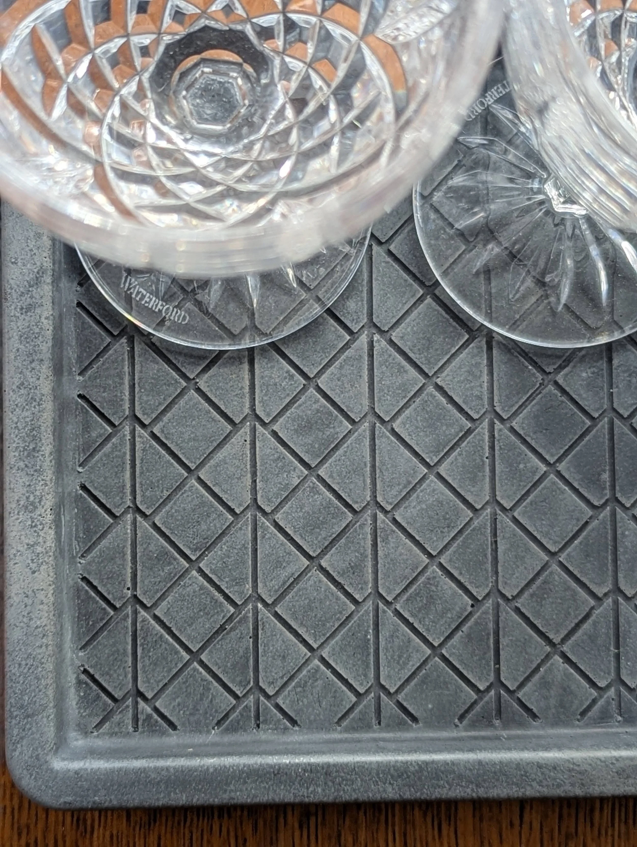 Three empty clear glass dessert cups on a black textured tray with a diamond pattern, on a wooden surface.